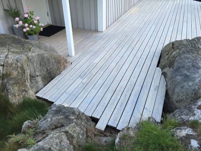 Vitpigmenterad träaltan omgiven av natursten, med en krukväxt vid en husvägg.