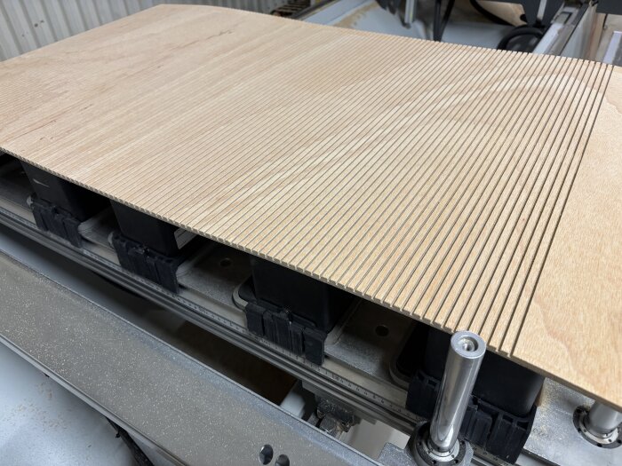 Skiva av plywood med sågade spår i en verkstad, klar för användning i byggprojekt.