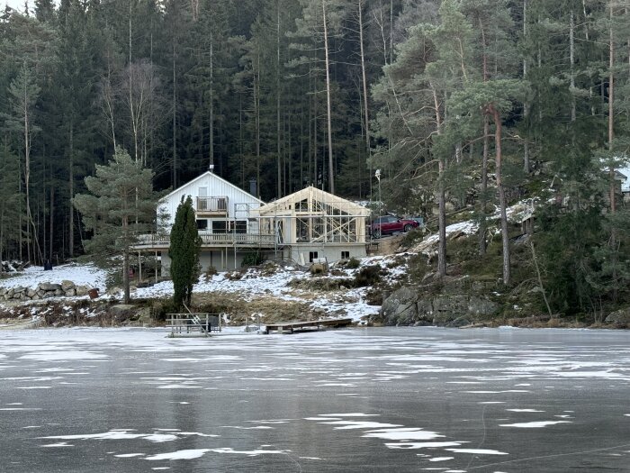 Hus vid skog i vinterlandskap med pågående renovering, halvfärdig byggställning och tillfälliga skyddsskivor under förberedelse för snöigt väder.