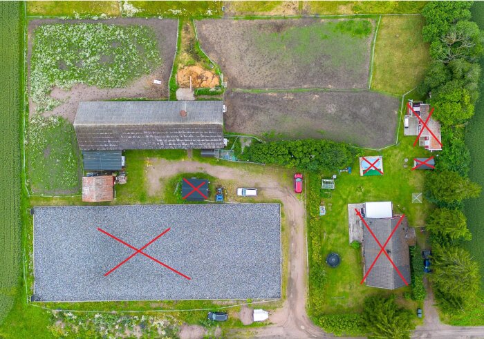 Flygbild av gård med flera byggnader markerade med röda kryss. Omgiven av åkrar. Högspänningsledning begränsar byggen.