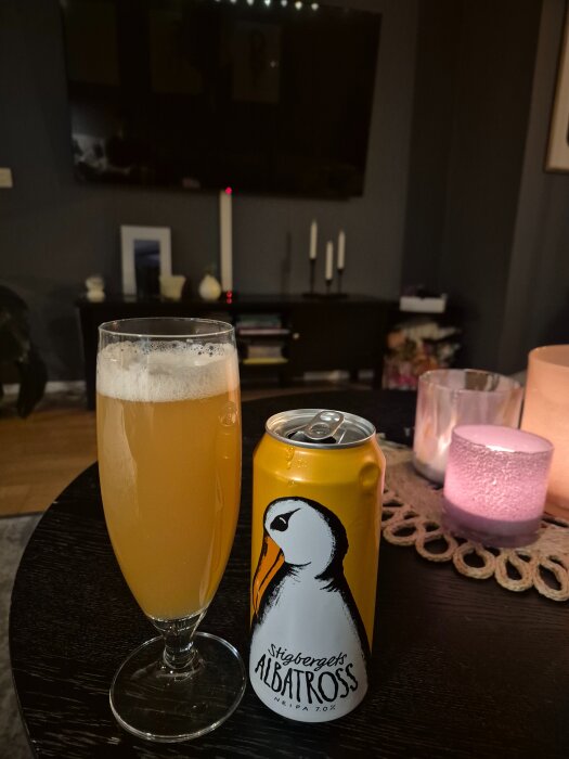 Ölglas med skummande, gyllene öl bredvid en gul burk med texten "Stigbergets Albatross" på ett mörkt bord, omgiven av ljus.