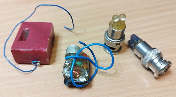 Fyra elektroniska komponenter, inklusive en röd FM-sändare och en effektivare sändare, visas på ett träbord tillsammans med andra enheter.