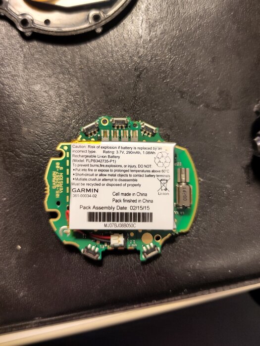 Garmin Fenix 3 kretskort med etikett om batterisäkerhet, modell och tillverkningsdatum, borttagen från höljet för reparation eller batteribyte.