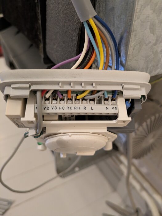 Kopplingsplint med flera färgade kablar anslutna till en Carrier 42NM fläktkonvektor, inklusive terminaler märkta V2, V3, H, R, C, R, H, L, N, V.
