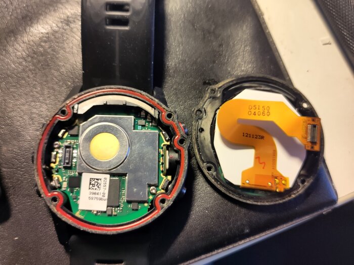 Invändig vy av en isärskruvad smartklocka med moderkort och skärm lossade, synlig flexkabel och T6-skruvar.