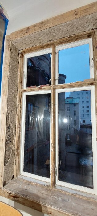 Renovering av fönstersmyg i sekelskifteslägenhet, med borttagen puts och exponerat trä runt fönsterkarmen, redo för omputsning och målning.