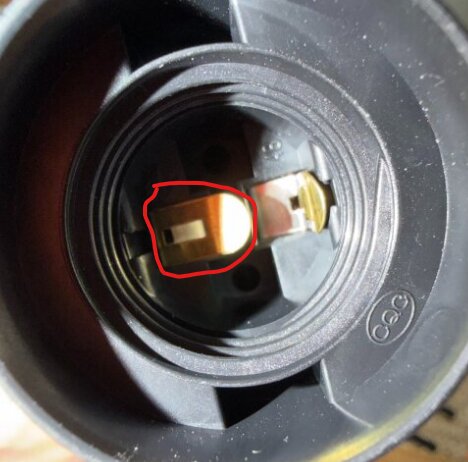 Inringad bild av en ljussockel med böjt bleck som kan orsaka kortslutning vid montering av lampa.