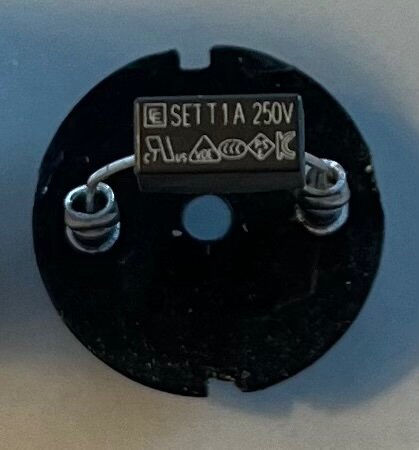 Säkringsliknande komponent från en gammal armatur, märkt "SET 1A 250V", visar märkningar och symboler relaterade till säkerhetsstandarder.