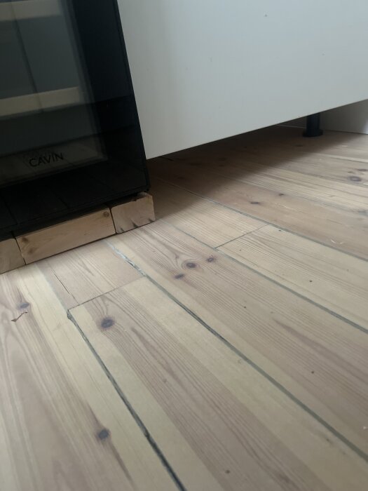 Vinkyl står på trälappar i kök med ljusa träplankor och en vit Ikea Metod-stomme synlig i bakgrunden.