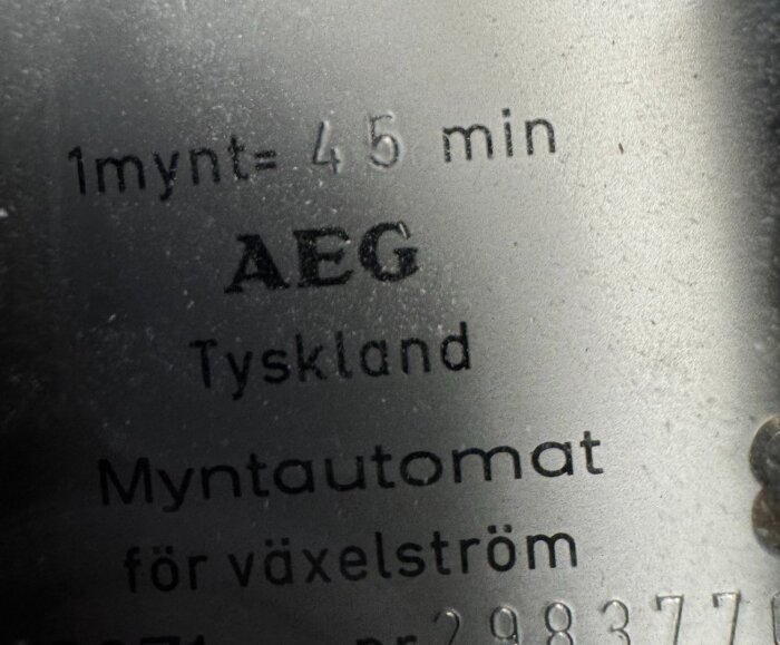 Myntautomatens märkplåt från AEG visar "1 mynt = 45 min" och att den kommer från Tyskland för växelström.