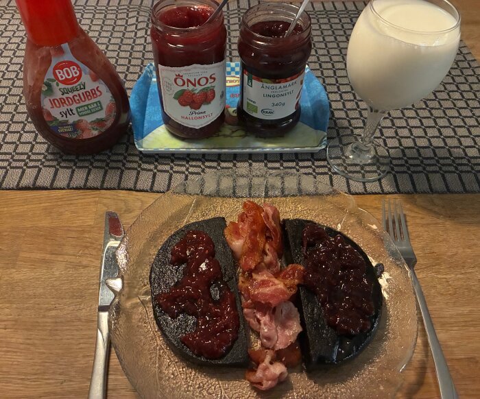 Blodpudding med sylt och bacon på tallrik med glas mjölk och syltburkar i bakgrunden.