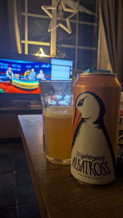 Ölburk och glas på bord framför TV som visar sportprogram i fjällstuga.