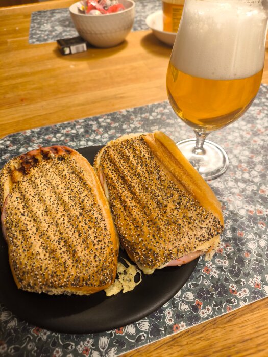 Två grillade toast med skinka, ost och stark tacosås på en tallrik bredvid ett glas skummande öl på matbordet.