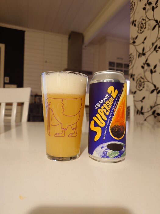 Ett glas med öl bredvid en ölburk på ett vitt bord i ett kök.