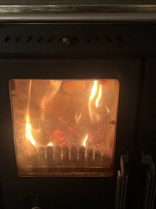 Vedeldad kamin med eld som brinner bakom glaslucka.