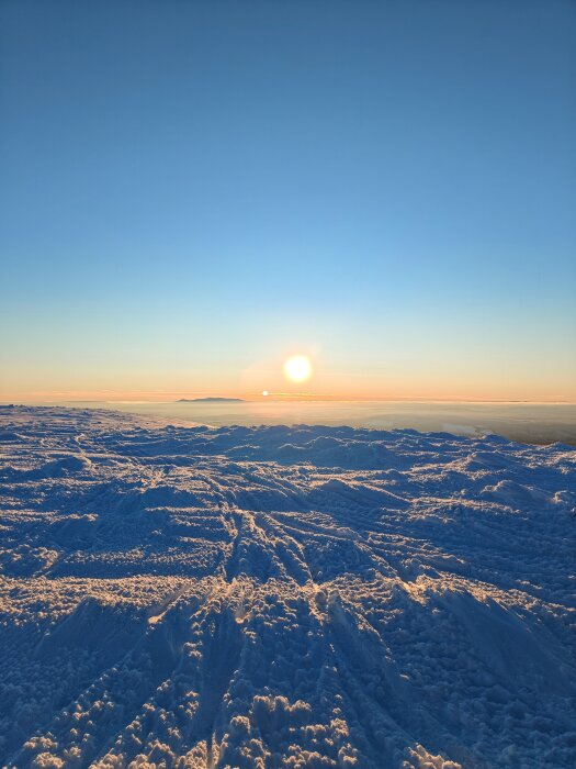 Solnedgång över ett snötäckt bergslandskap, med djupa skuggor och ett klart blått himmel i bakgrunden.