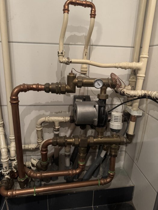 Rörsystem med kopparrör, ventiler och termostat, inklusive en rund vit termostat, i en väggmonterad installation.