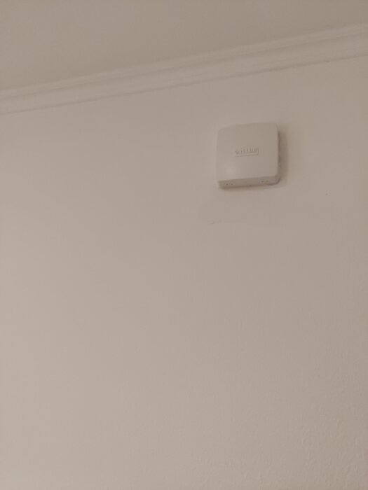 Vitt ventilationsgaller monterat på en ljus vägg nära taket.