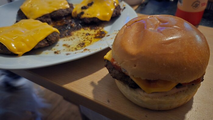 Hamburgare med smält ost på ett fat och i ett bröd på bord.