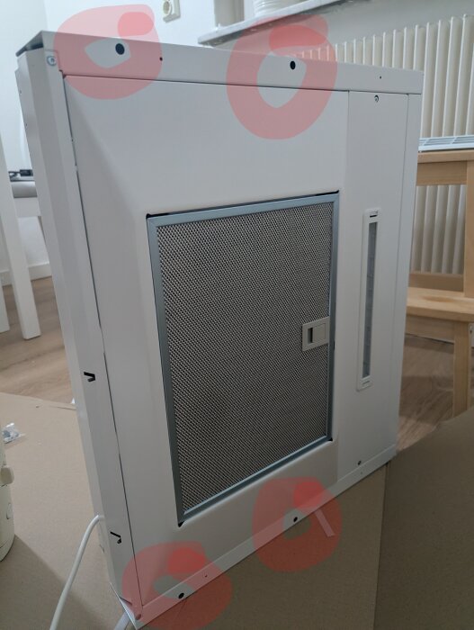 Vit köksfläkt av märket Cylinda Popular FK260C, med synlig metallfilter och hålmarkerade för montering, stående i ett rum med ljus interiör.