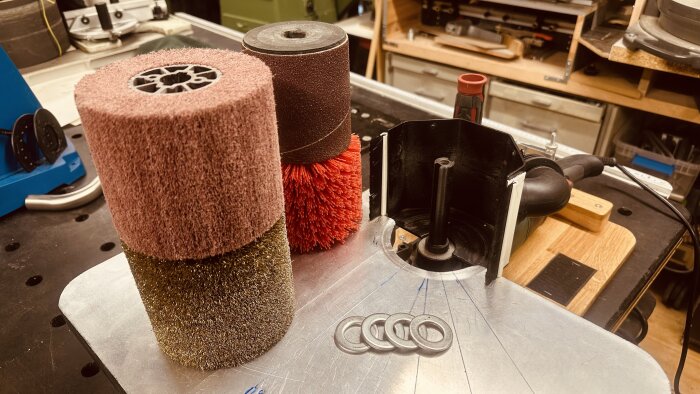 Verktygsrullar och brickor på en garrotterings-jigg i en verkstad, med varierande diametrar och materialtexturer.