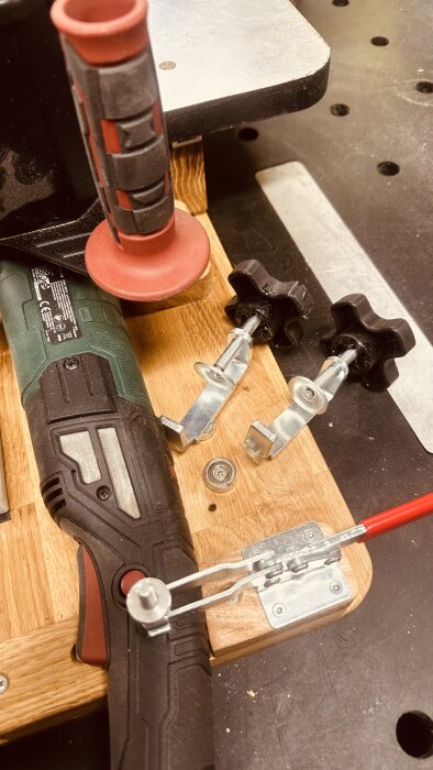 Verktyg på arbetsbänk med en slipmaskin och metallklämmor för garrottering, inzoomat på detaljer och handtag.