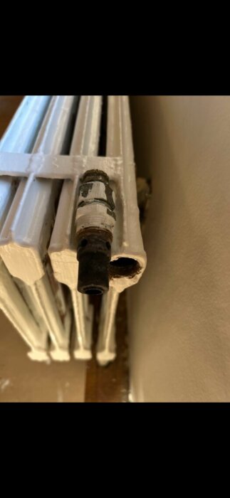 Gammal vitmålad radiator med trasig termostat utan hatt, sedd från sidan mot en vägg.