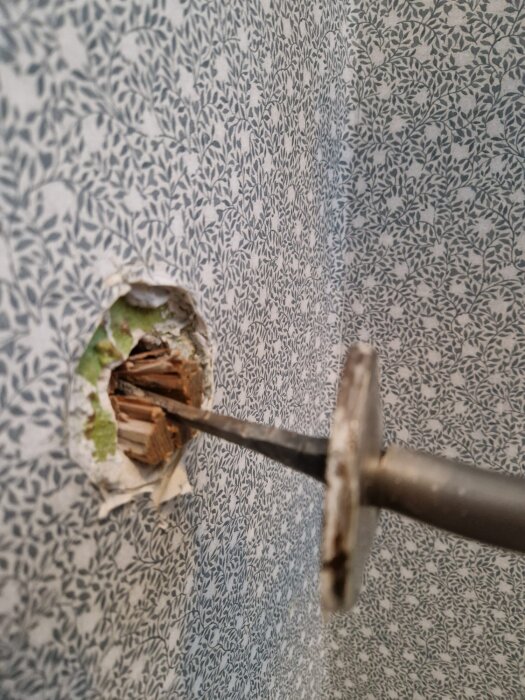 Löst trappräcke med skruvmejsel insatt i väggöppning, tapet med lövmönster, fråga om fastsättning.