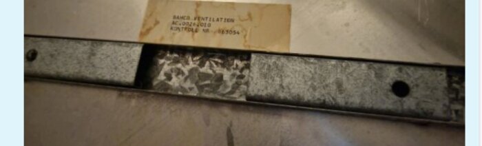 Närbild på plattvärmeväxlare med metallram och etikett med text om Sandbö ventilation.