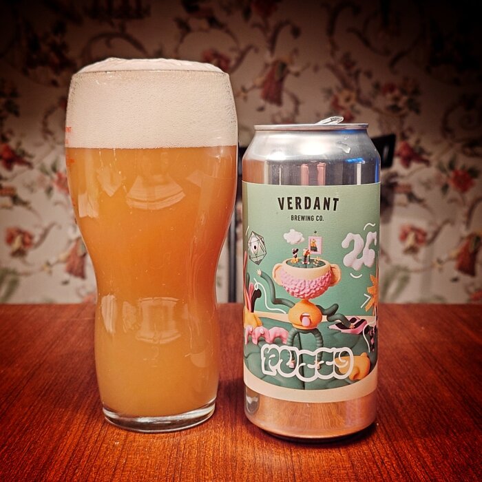 Ett glas med skummig hantverksöl bredvid en färgglad ölburk från Verdant Brewing Co. med fantasifull etikett.