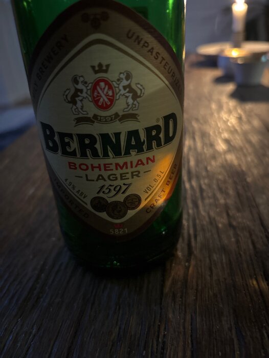 Flaska Bernard Bohemian Lager på mörkt träbord, etikett med lejon och kungakrona syns tydligt.