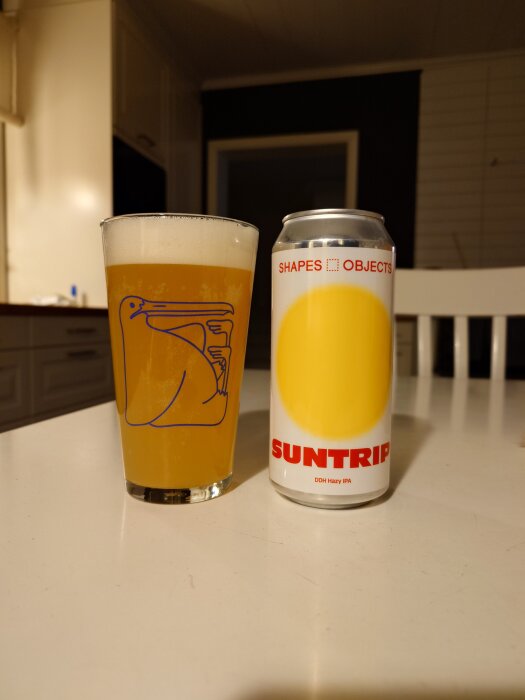 Glas med öl bredvid en burk märkt "Shapes & Objects Suntrip DDH Hazy IPA" på ett bord i ett kök.