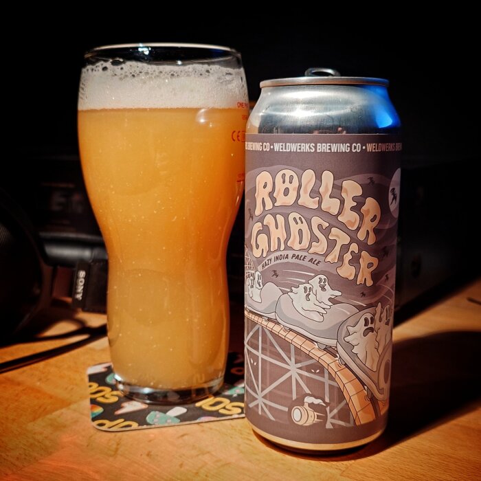 Ölburk med etikett "Roller Ghoster" bredvid ett glas fyllt med ljus öl på ett bord.
