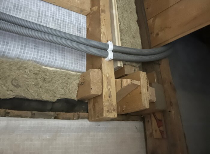 Isolering och ångbroms syns på vinden, med innerväggsstruktur i trä och två gråa rör monterade ovanpå konstruktionen.