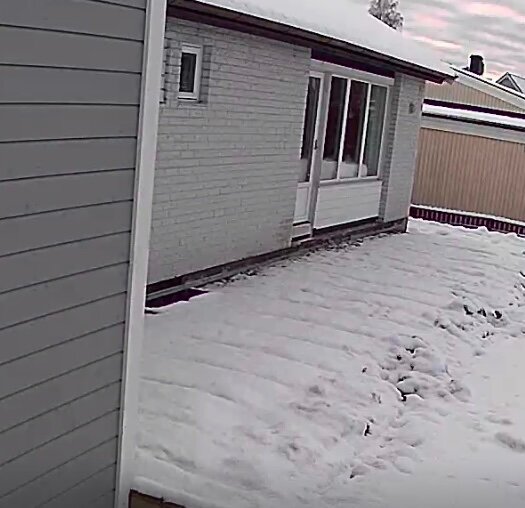 Vit tegelbyggnad med stora fönster, snötäckt mark framför. Altan borttagen, man ser husgrund och ljusbrunnar, innan grävningsarbete.