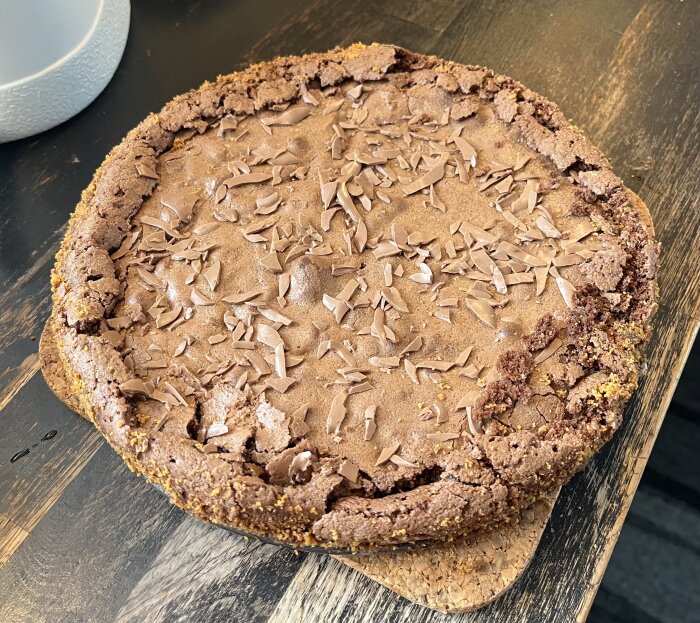 Hemlagad kladdkaka toppad med chokladspån på ett träbord.