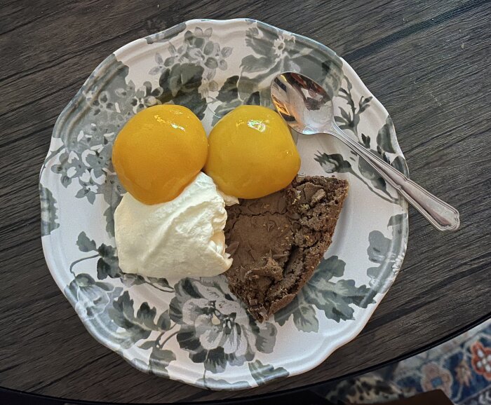 Kladdkaka med grädde och konserverade persikor på en mönstrad tallrik, med en sked vid sidan.