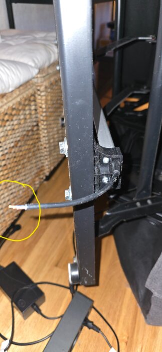 En trasig kabel som hänger från en mekanisk arm i ett rum med trägolv och korgmöbler.