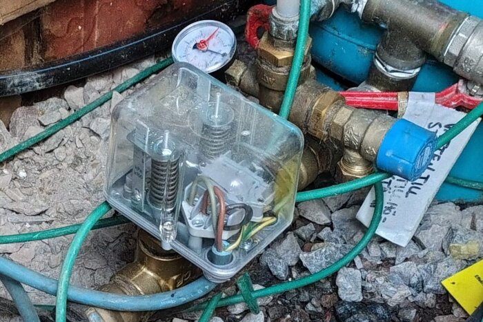 Tryckströmbrytare och manometer med anslutna slangar och rör vid privat brunn.