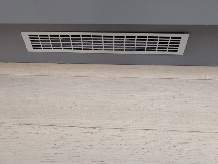 Ventilationsgaller installerat vid golvlist för att främja luftcirkulation, med pågående läckageproblem.