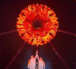Två personer står under en stor, lysande röd-orange skulptur eller installation på natten.