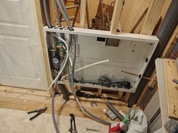 Fördelarskåp med rörinstallationer i rum under renovering, verktyg och material synliga på trägolv.