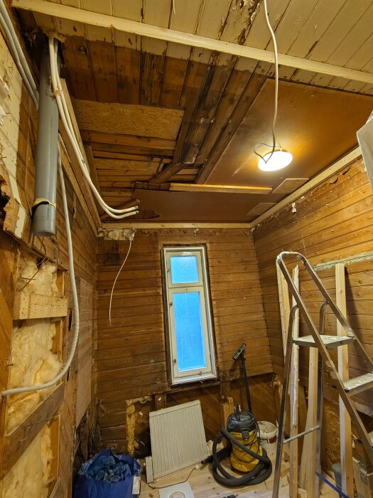 Rum under renovering med träväggar, stege, golv och fönster. Golvet är färdigt och tvättrummets avlopp klart.