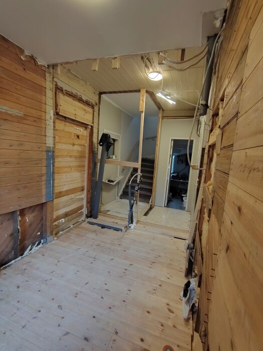 Renovering av rum med nytt trägolv och synliga träväggar, ofärdigt tak och öppning mot entré och trappa.