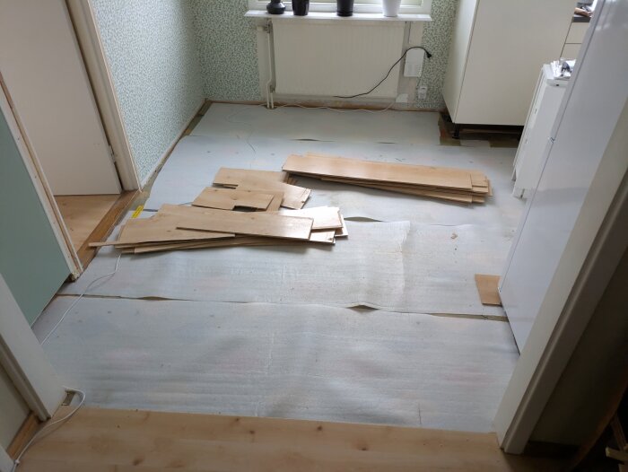 Brutet golv med träbrädor från husrenovering, exponerande äldre underlag i köksområde.