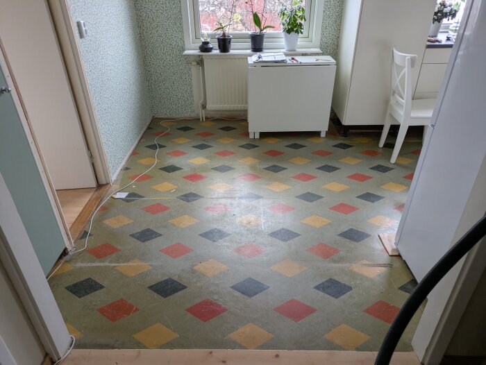 Golv från 60-talet uppenbarat efter rivning, med färgglada mönster i rött, gult och svart i ett rum med gröna väggar och vita möbler.