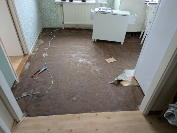 Gamla golvet från 60-talet är synligt efter att ha rivits upp; trasor, verktyg och brädor ligger utspridda i ett rum med retroinredning.