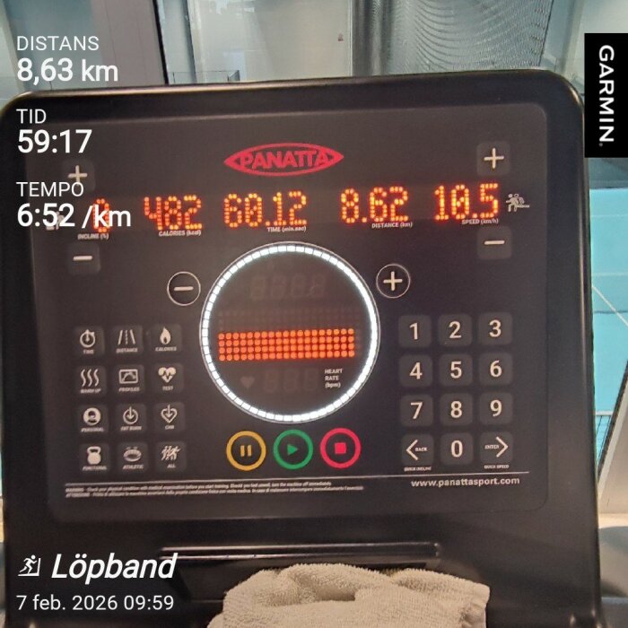 Kontrollpanel på ett löpband med träningsstatistik: 8,63 km distans, 59:17 min tid, 6:52 min/km tempo, synlig handduk.