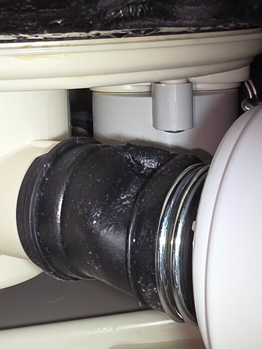 VVS-installation med avloppsrör och svart packning i närbild, synligt under diskbänk, visar röranslutning och tätningsdetaljer.