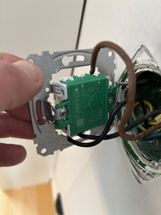 Närbild av en person som installerar en grön strömbrytare med flera kopplade kablar inuti en vägg.